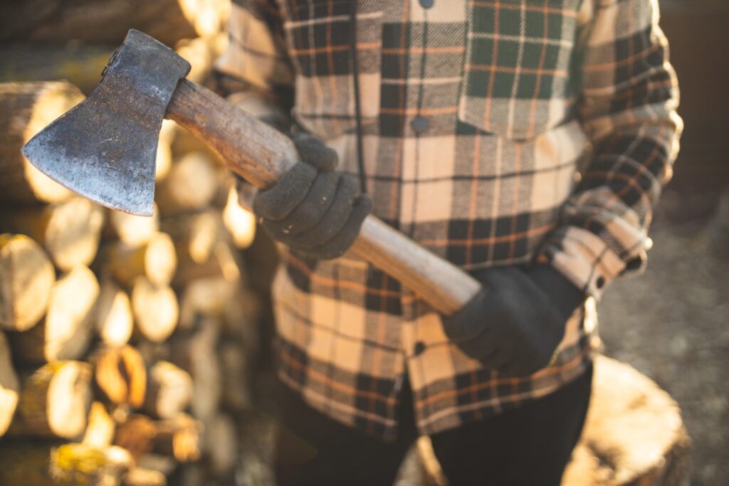 A man in a flannel shirt standing outdoors holding an axe.