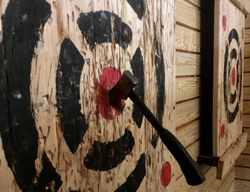 An axe sticking out of a wooden target board at an axe throwing range.