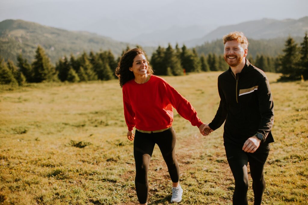 Smiling couple walking through a grassy open field near a forest.