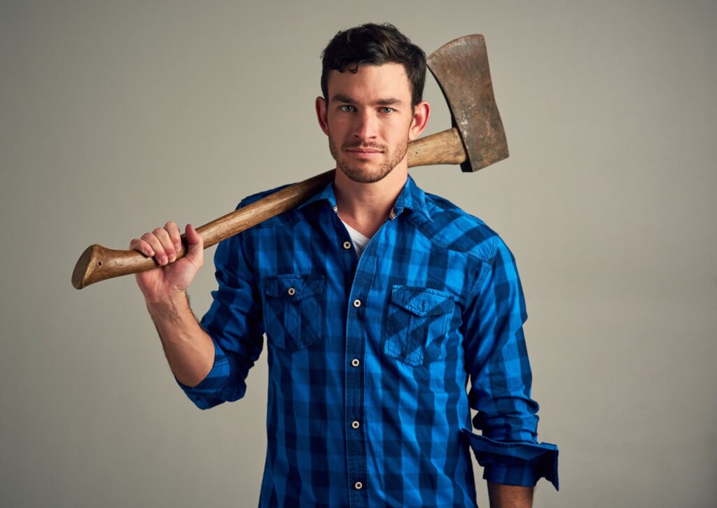 A man in a blue plaid shirt holds an axe over his shoulder.