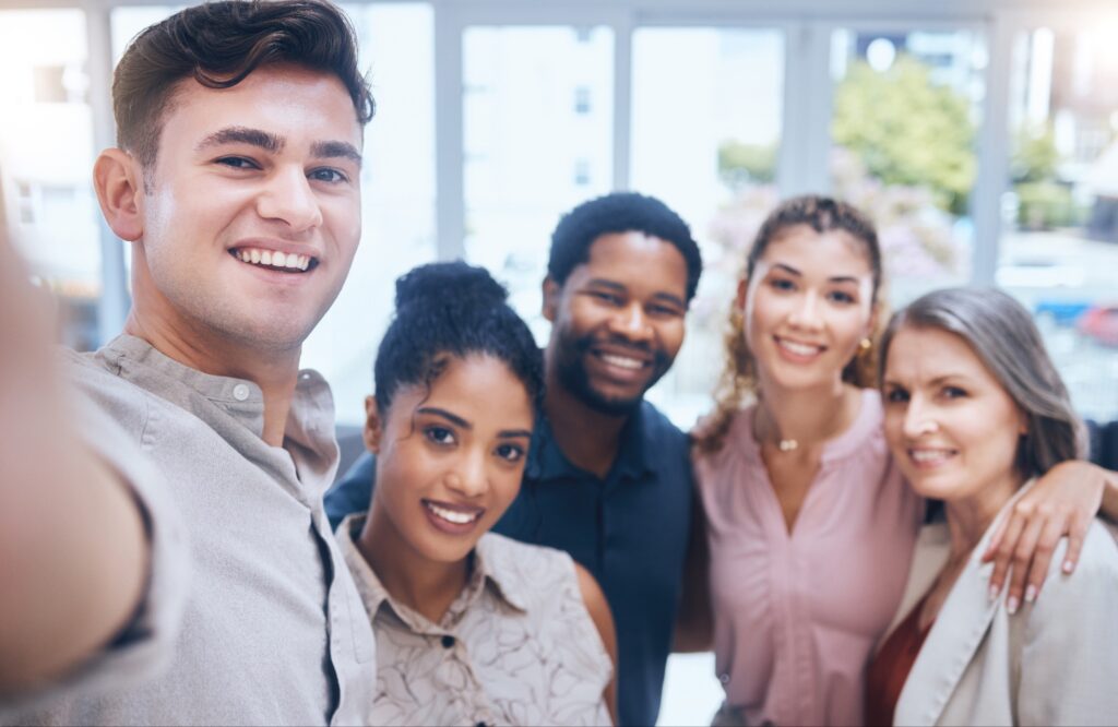 A group of people stands together for a group selfie in an office setting.