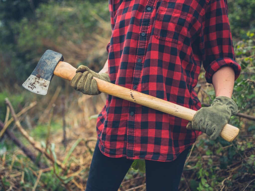 Person with gloves holding an axe outside next to shrubbery.