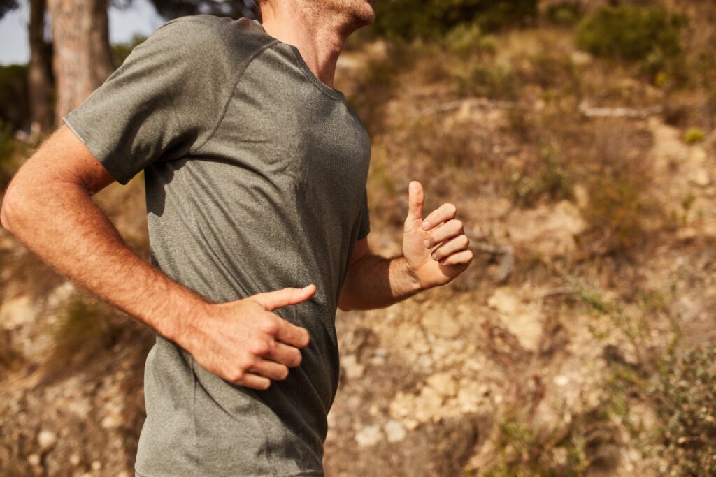 A view of a man’s torso as he runs on a trail through a park.