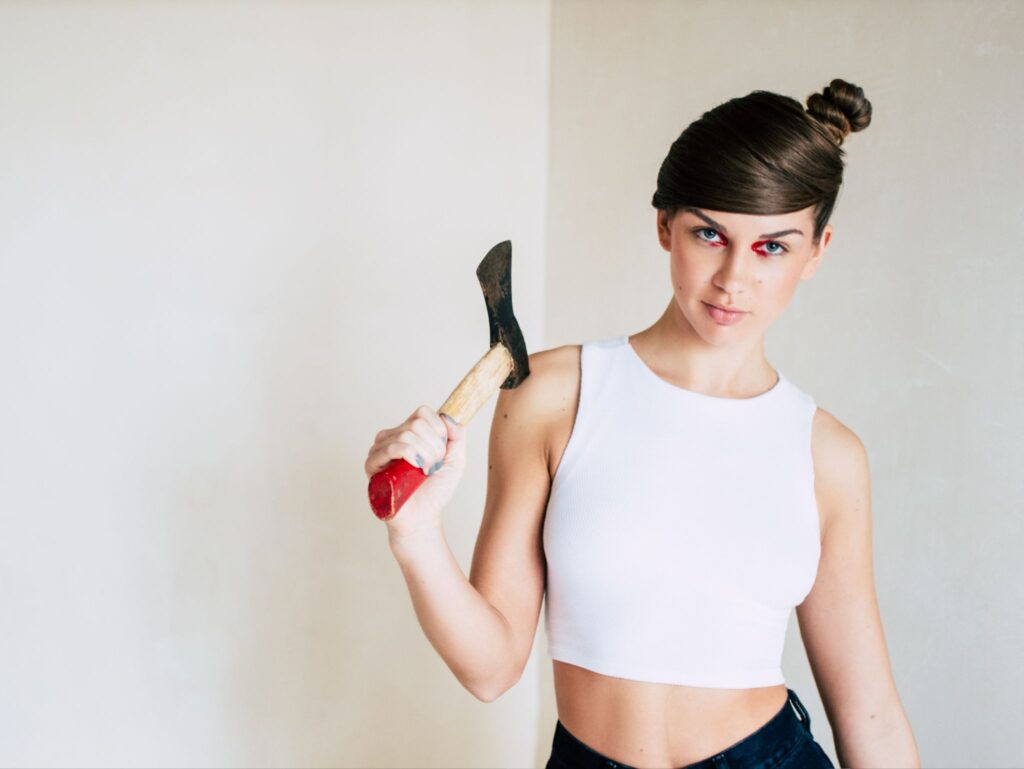 A young woman smiles and holds an axe over her shoulder.