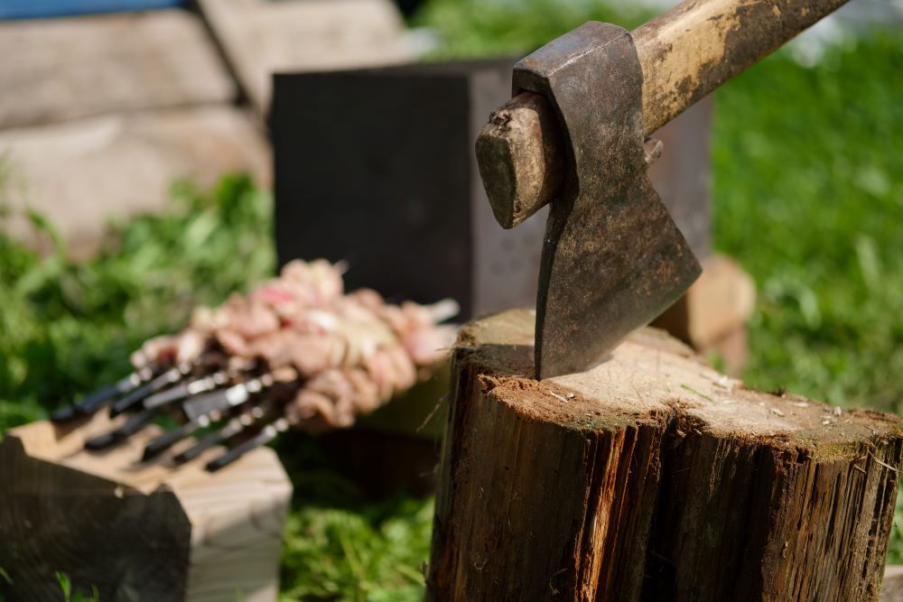 Axe stuck in a piece of wood with grass in the background.