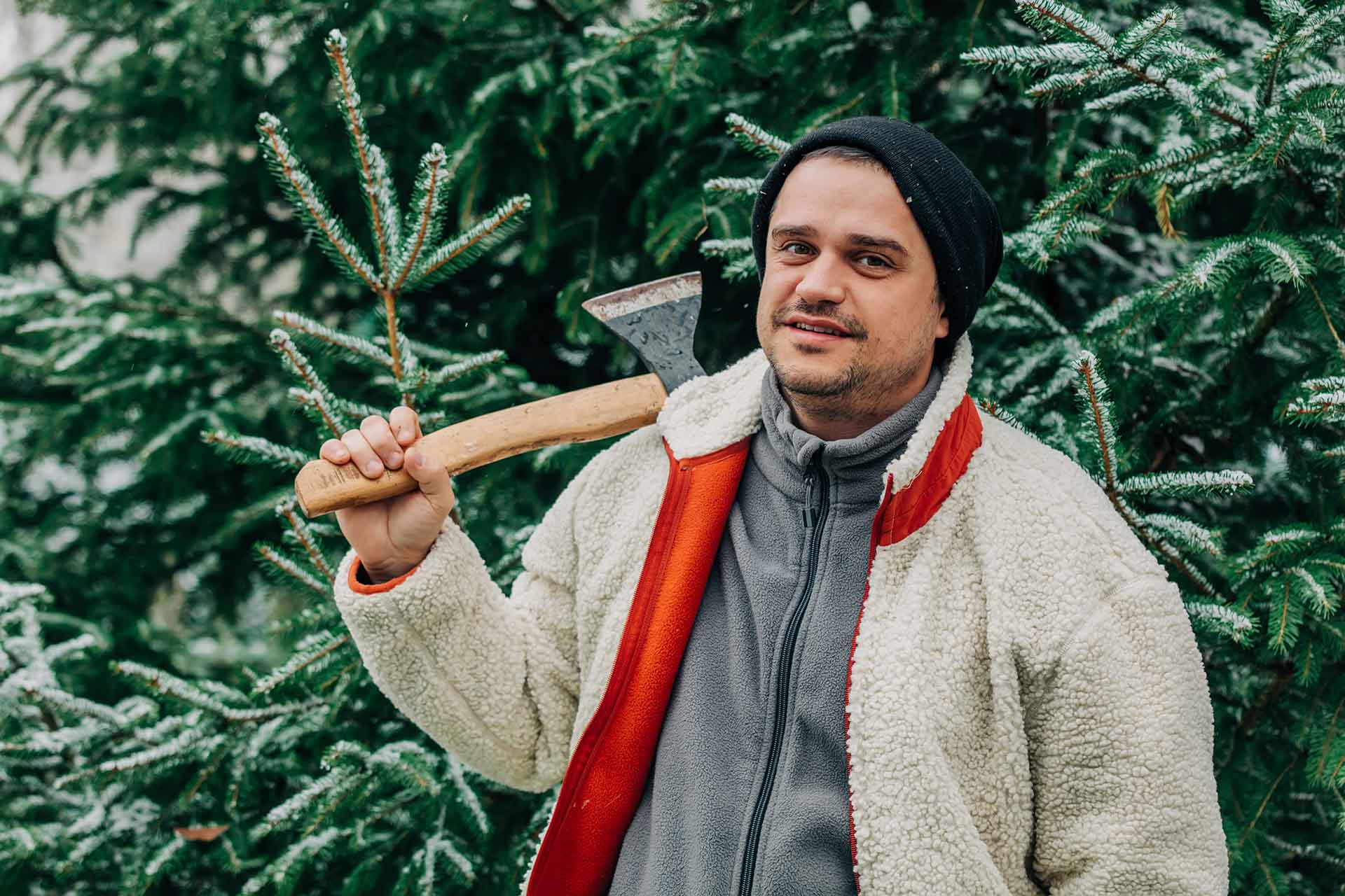 A man is holding an axe next to the Christmas tree.